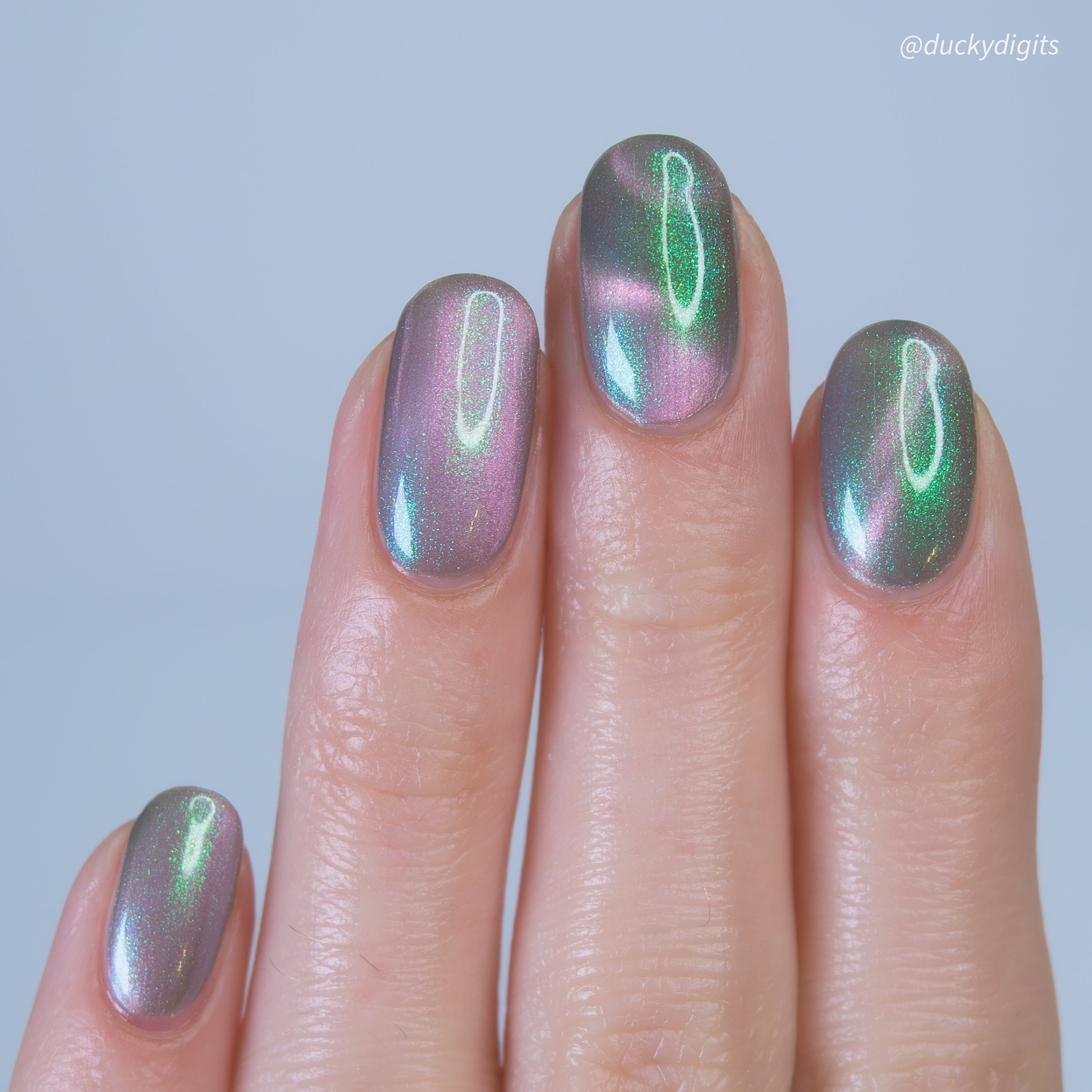 Nails with metallic green and pink polish on a neutral background