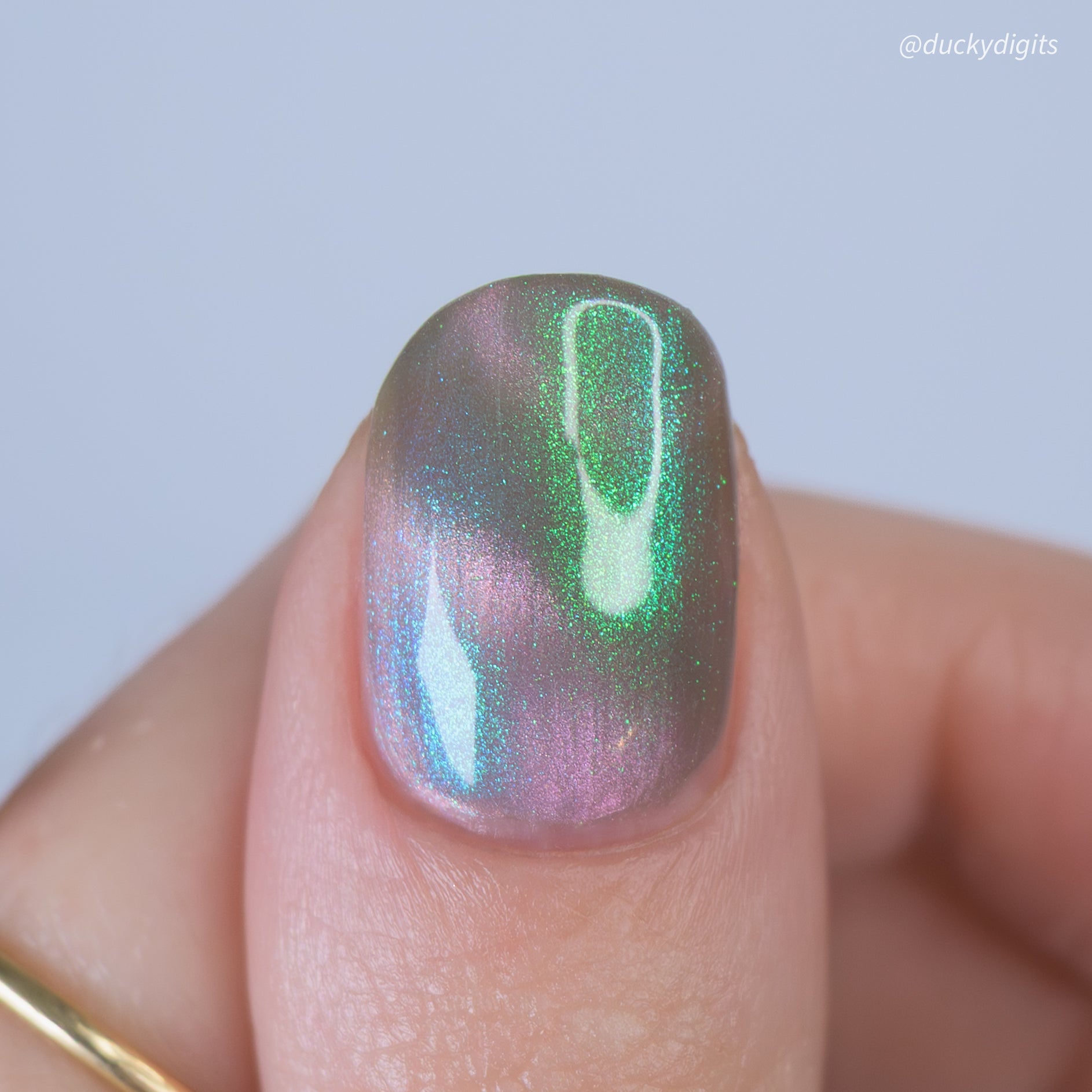 Nail with iridescent green and purple polish on a light gray background
