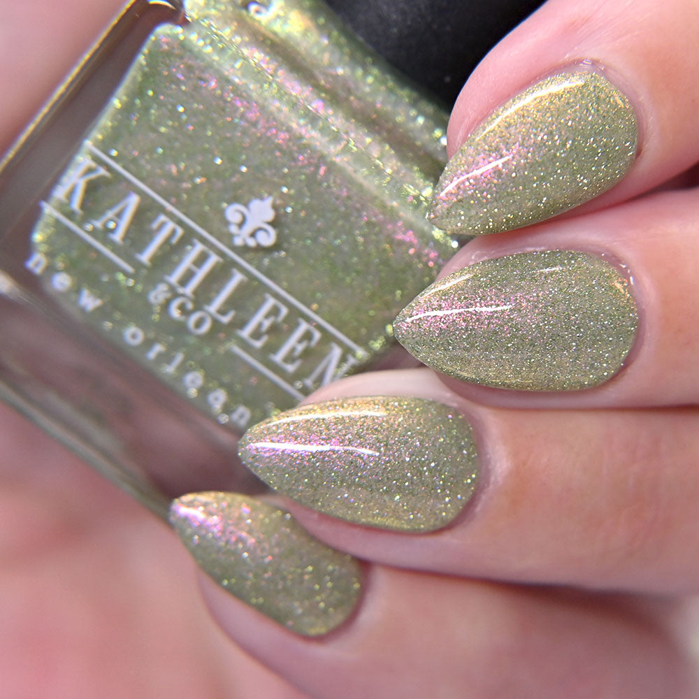 Nail polish with glitter green color held by a hand, showing brand &