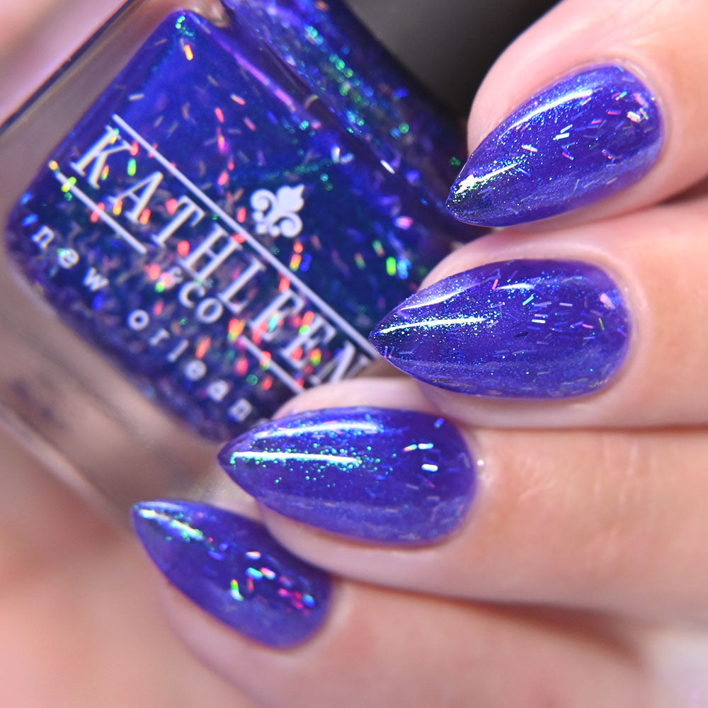Purple glittery nail polish on nails with a bottle of KATHLEEN CO. nail polish.