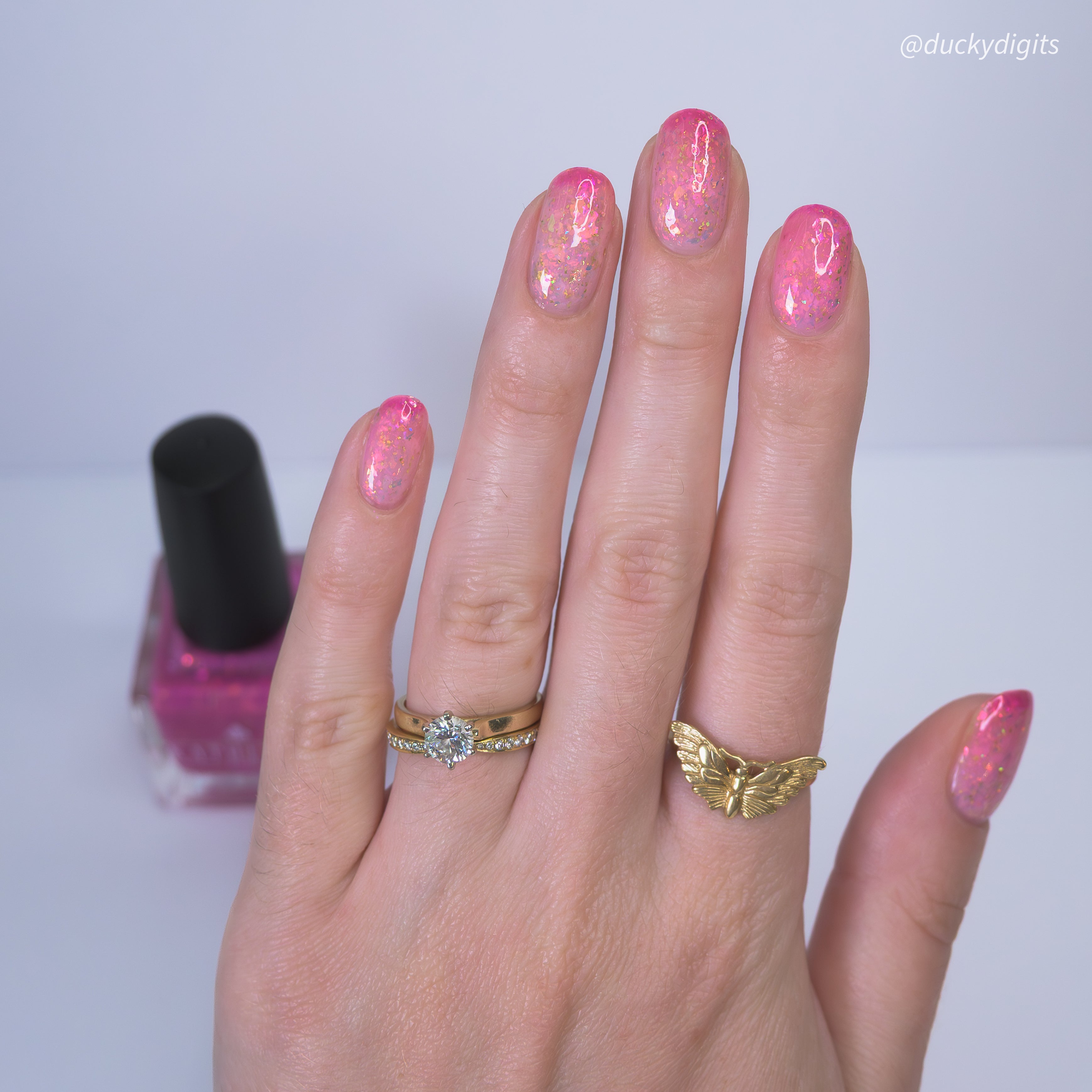 Hand with pink thermal nail polish and two rings, with a bottle of pink nail polish in the background.