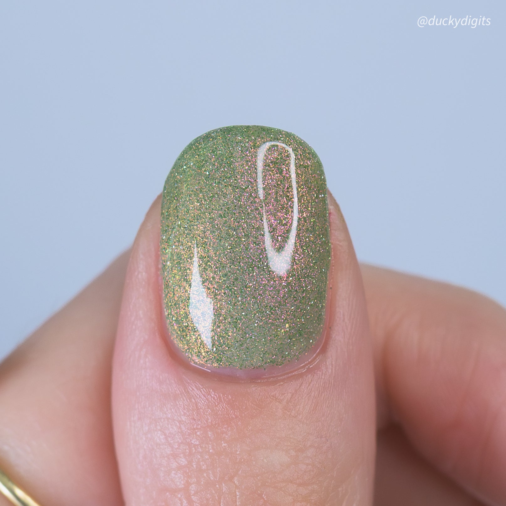 Nail with green glitter polish with pink shimmmer on a grey background