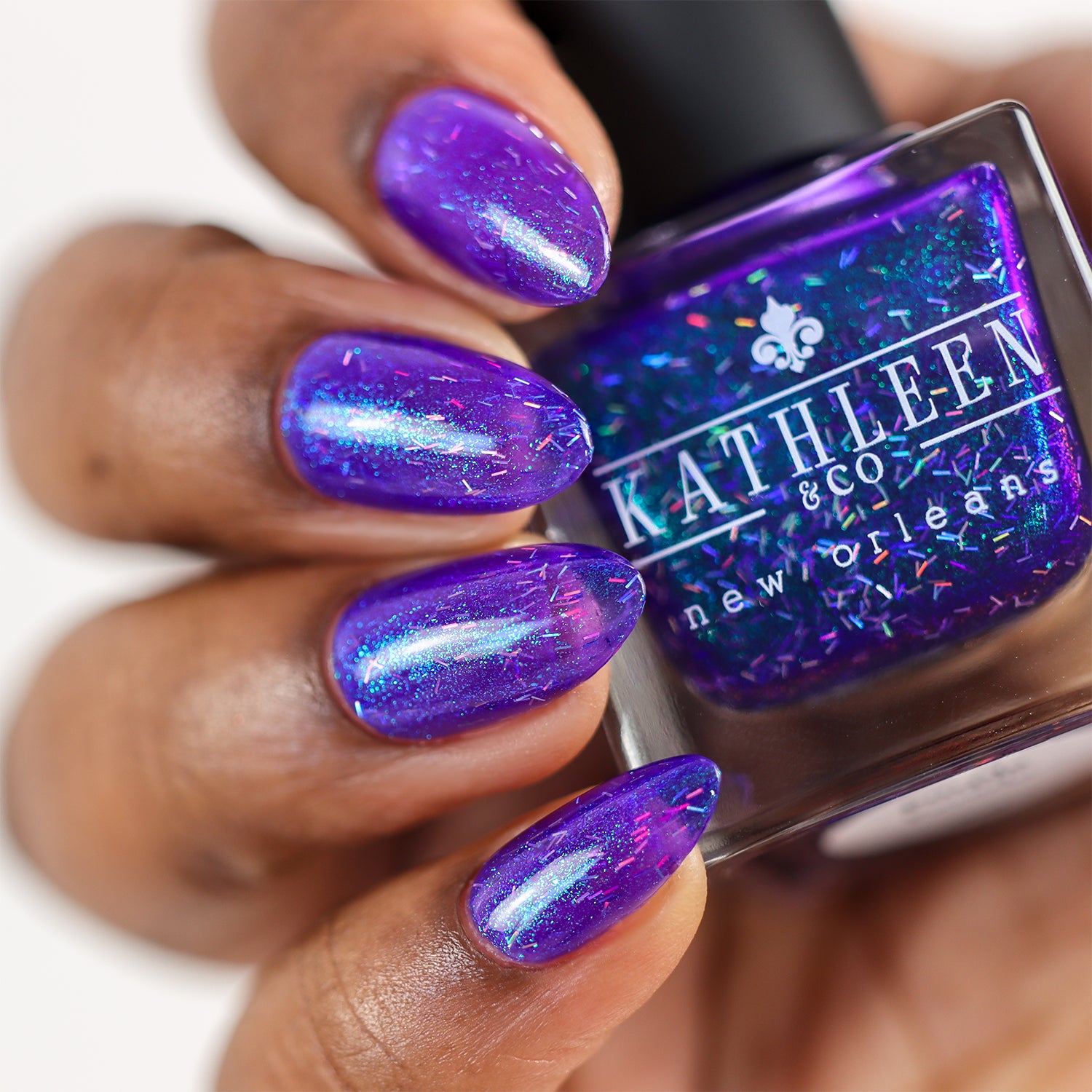Purple nail polish with glitter held by a hand, next to a bottle of Kathleen & Co New Orleans nail polish.