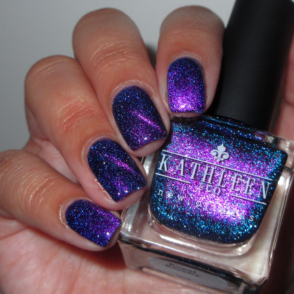 Hand with purple magnetic reflective glitter nail polish holding a bottle of Kathleen &amp; Co. nail polish.