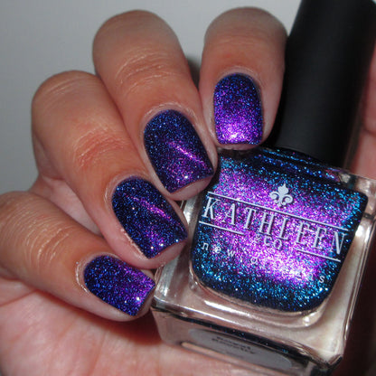 Hand with purple magnetic reflective glitter nail polish holding a bottle of Kathleen &amp; Co. nail polish.