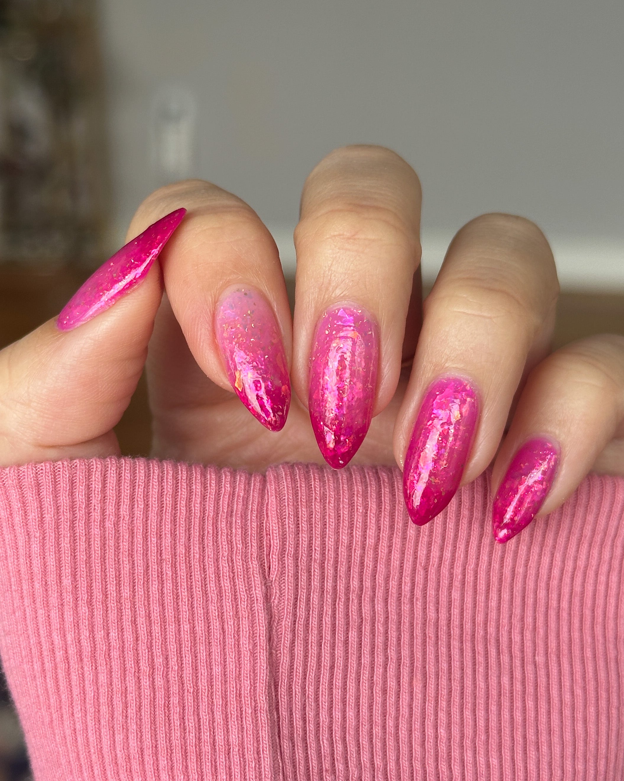 Close-up of a hand with pink thermal nail polish on a pink textured surface.
