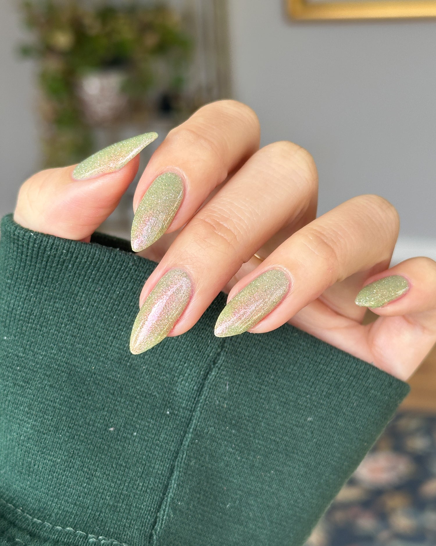 Close-up of a hand with green glitter nails wearing a green sleeve.