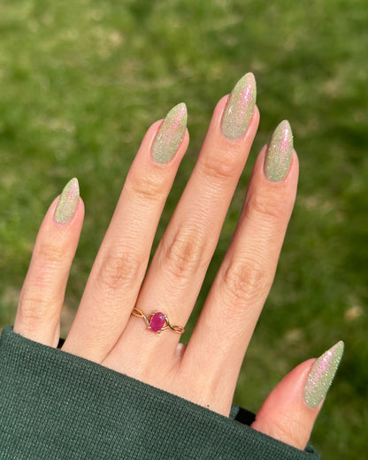 Hand with green reflective glitter nails wearing a ring on a blurred green background