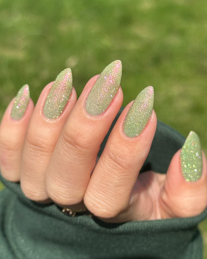 Close-up of a hand with green glitter nail polish against a blurred green background