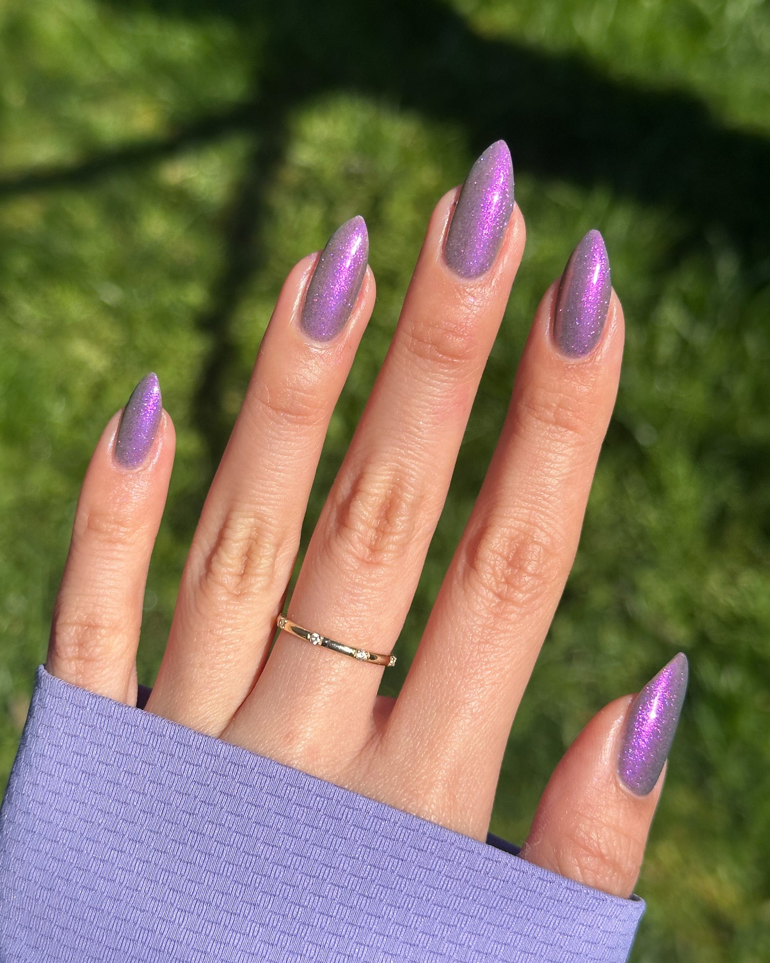 Hand with purple magnetic nails against a green grass background