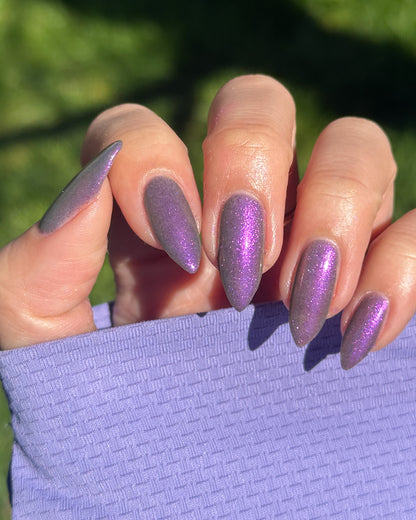 Hand with purple shimmer nail polish holding a purple fabric against a green background