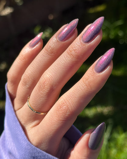 Hand with purple glittery nails against a blurred green background