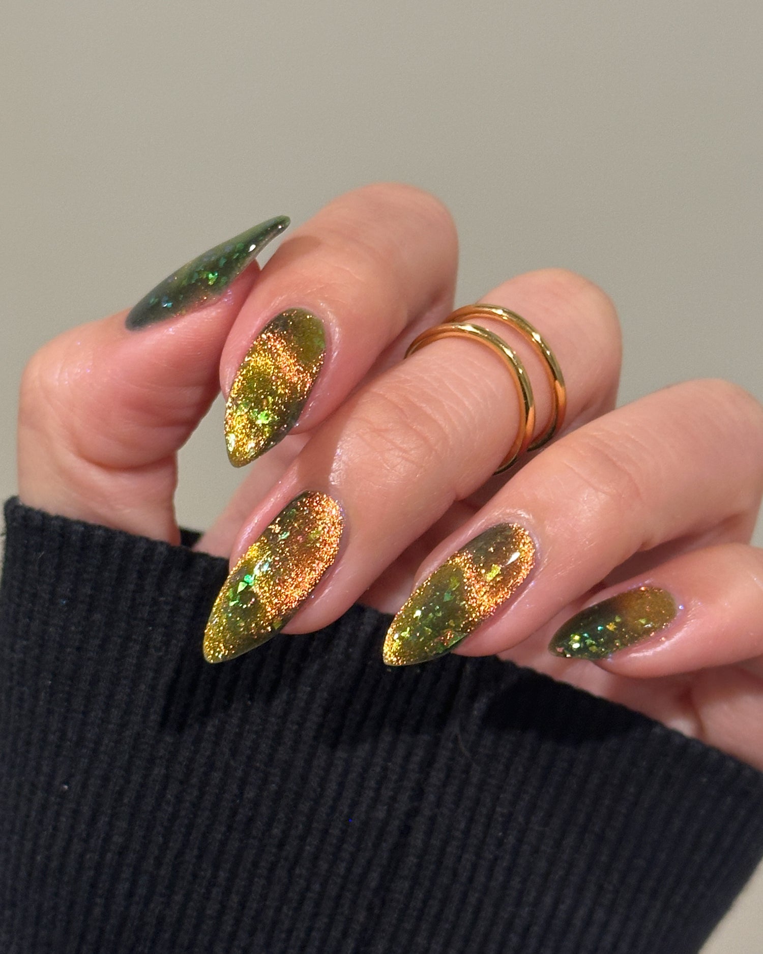 Hand with magnetic green and gold nails wearing a black sleeve.