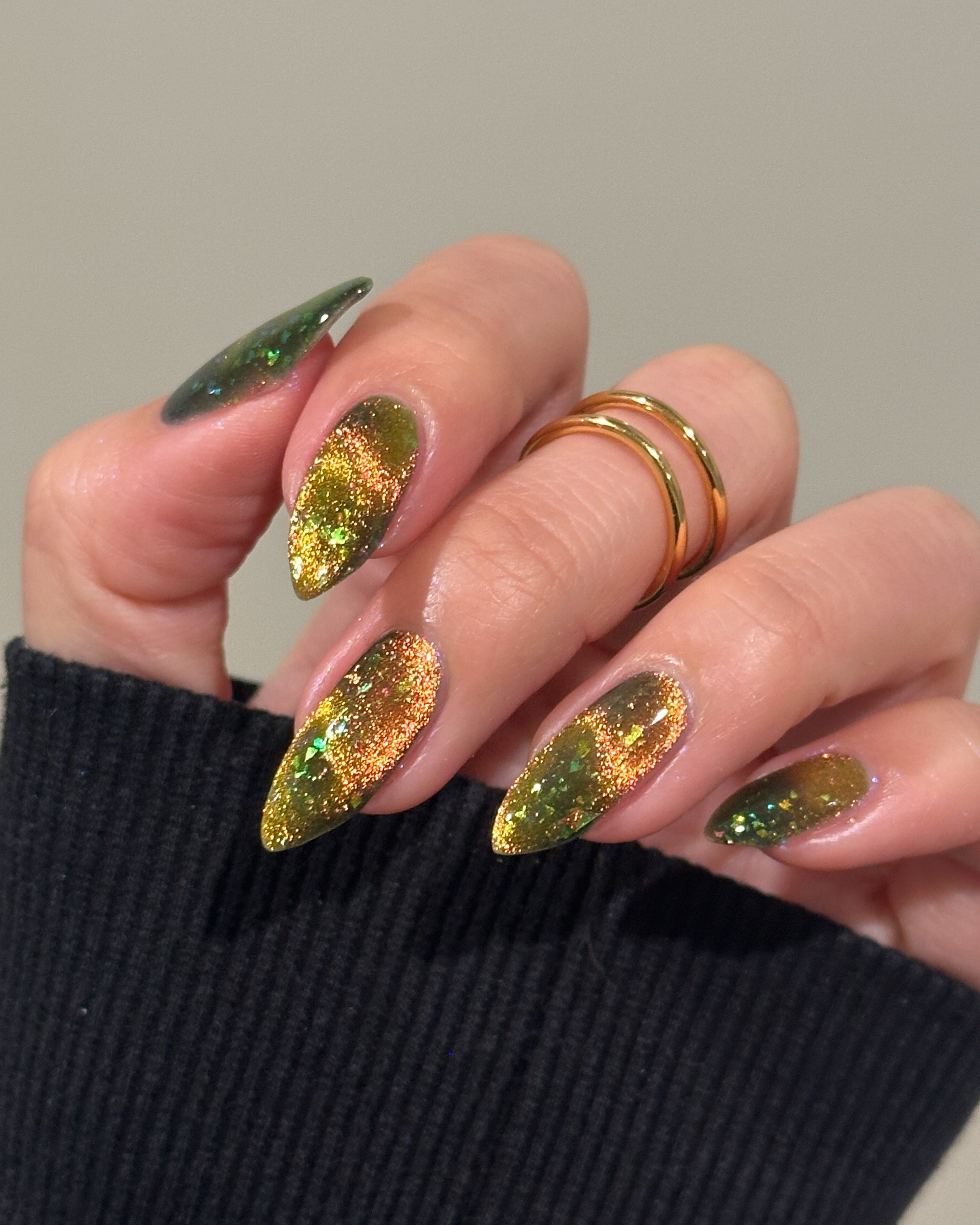 Hand with magnetic green and gold nails wearing a black sleeve.
