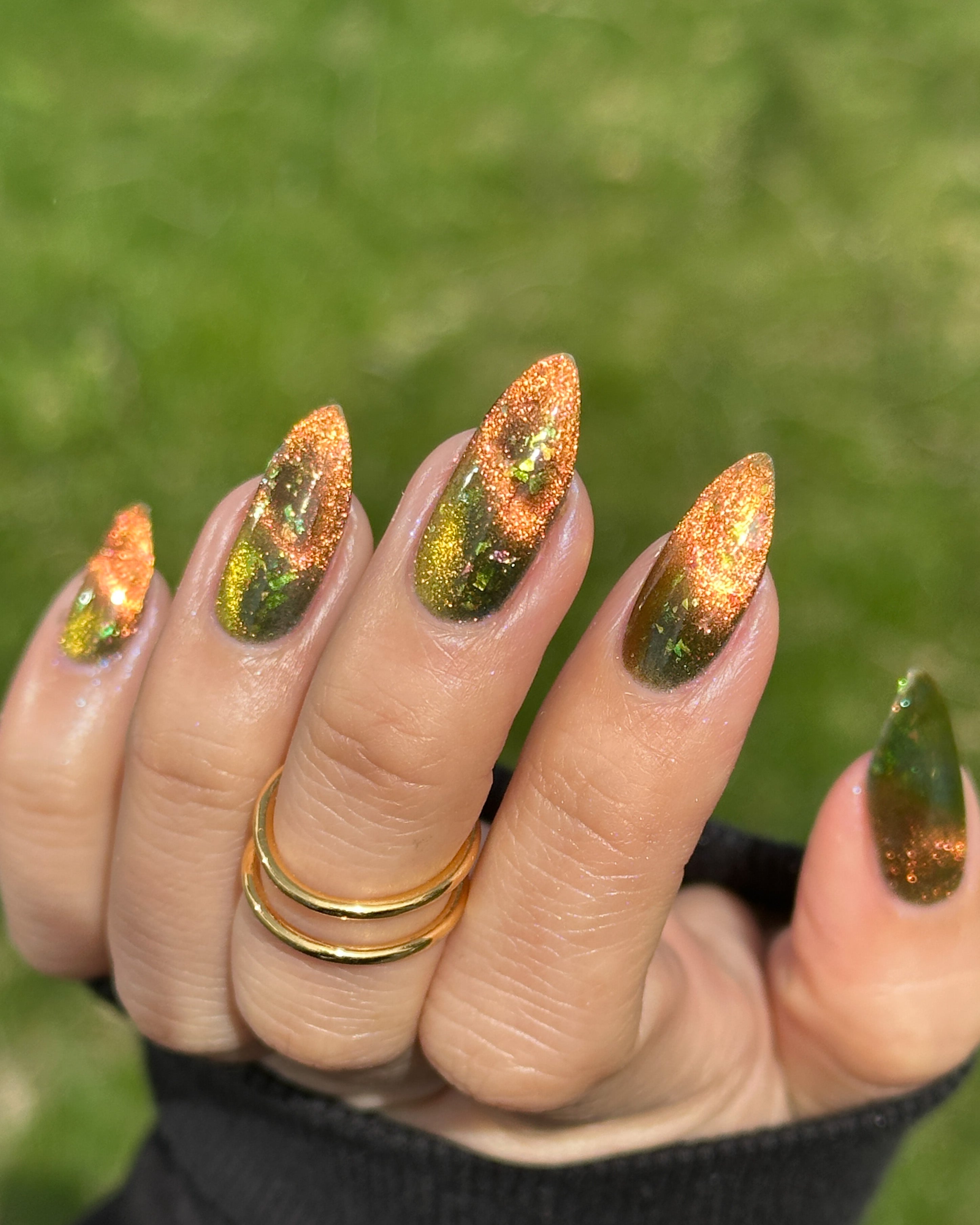 Nails with green and orange magnetic nail polish on a blurred green background
