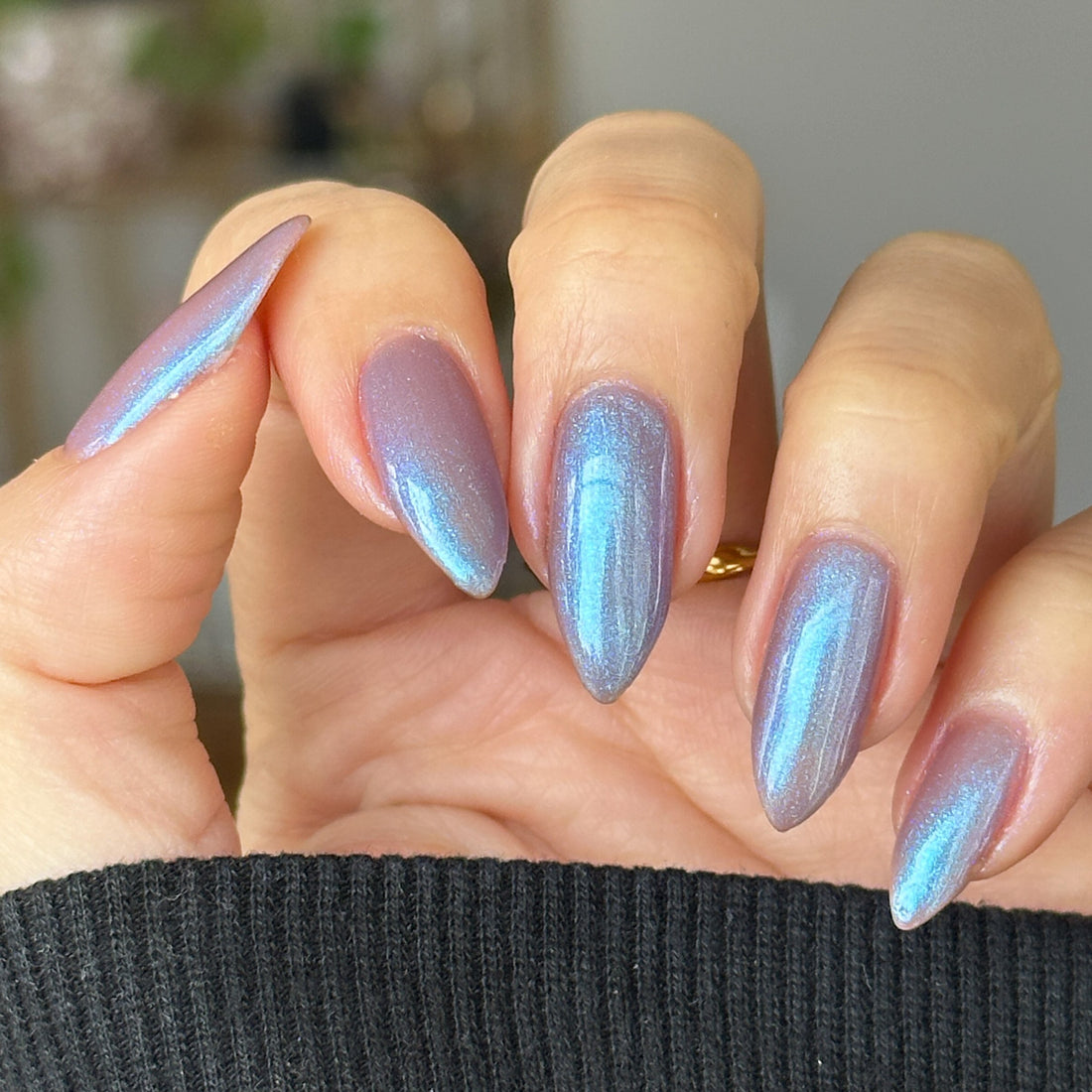 Hand with blue shimmer nail polish on a blurred indoor background
