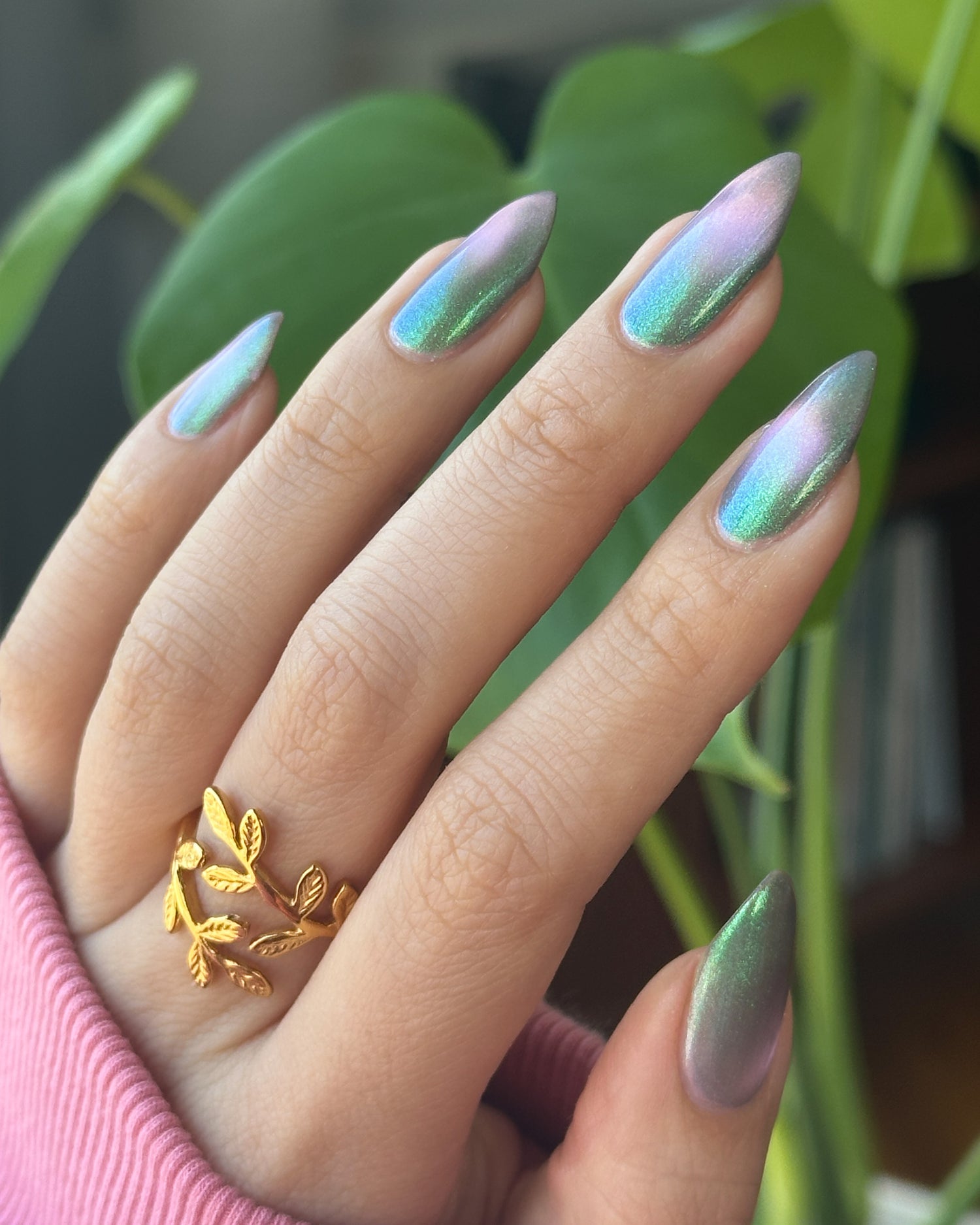 Hand with magnetic nail polish and a gold ring, against a green leafy background