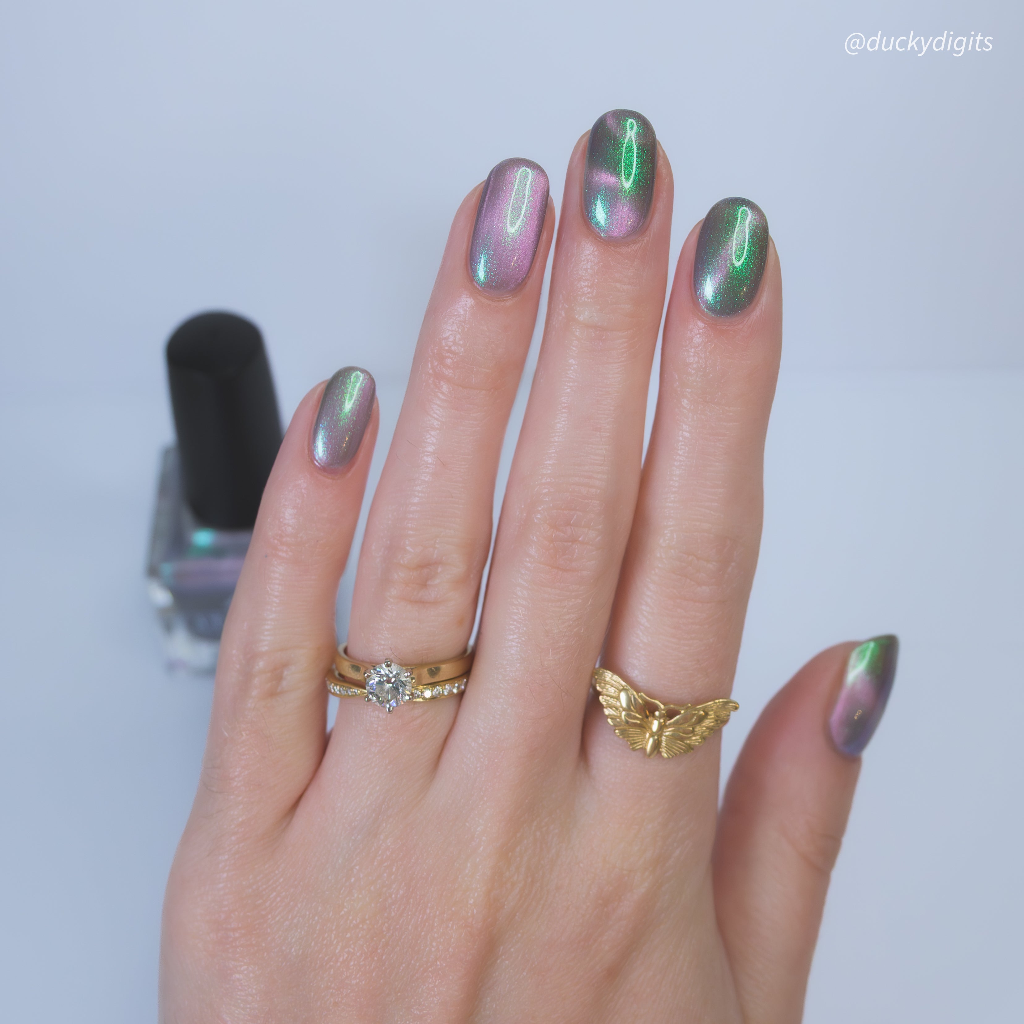 Hand with gold rings and magnetic nail polish on a light background