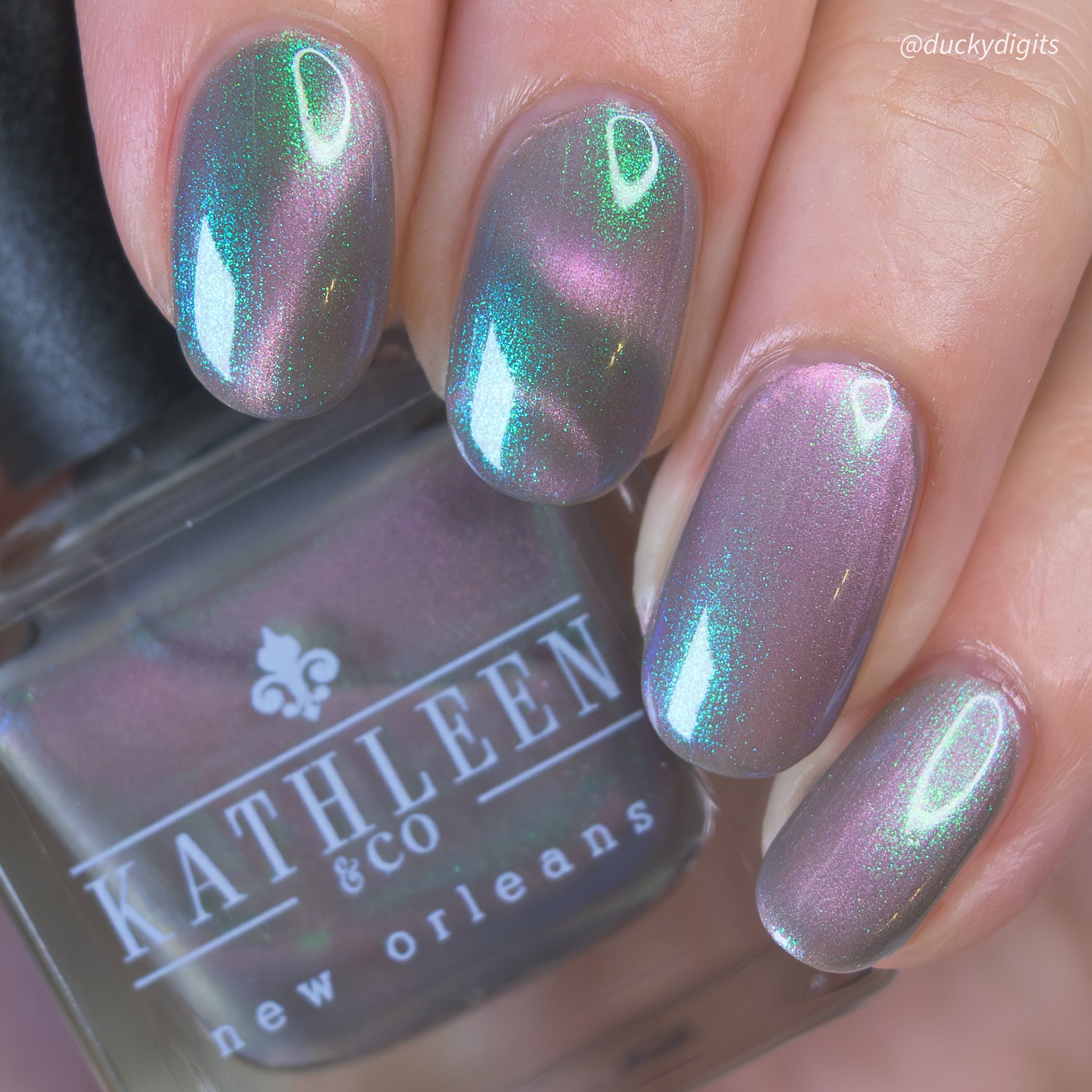 Nails with magnetic nail polish held against a bottle labeled &