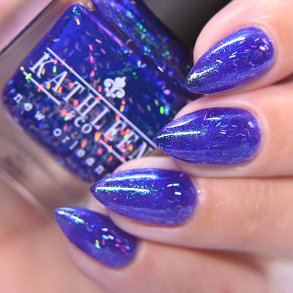 Purple glittery nail polish on nails with a bottle of KATHLEEN CO. nail polish.