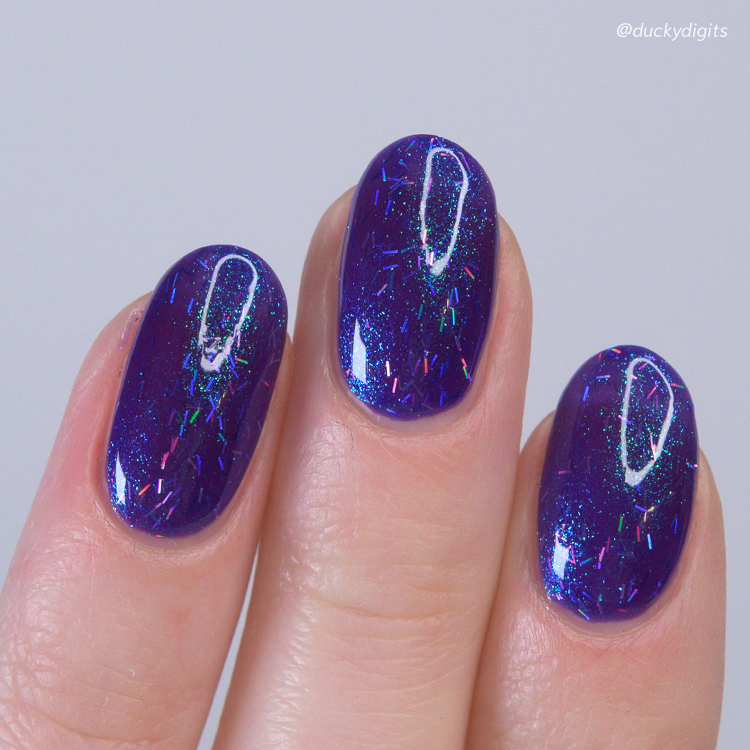 Close-up of a hand with purple glittery nail polish on a plain background