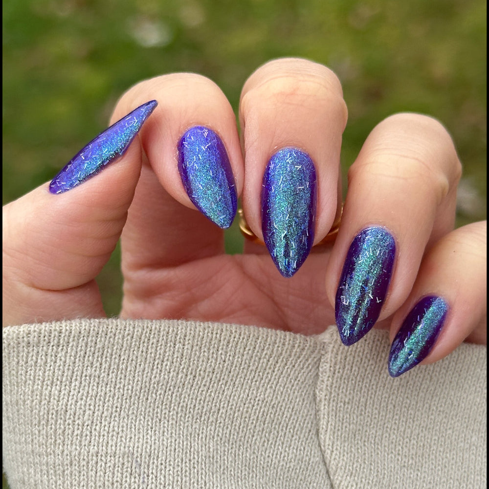 Hand with blue glittery nail polish against a blurred green background