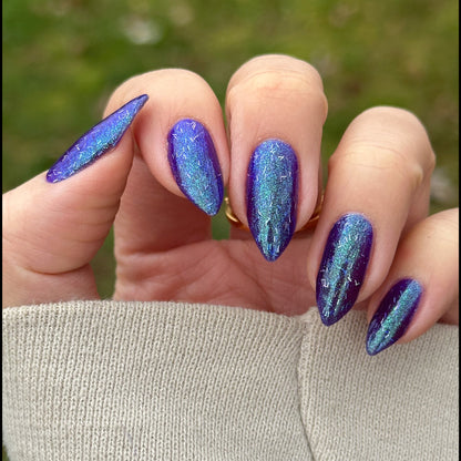 Hand with blue glittery nail polish against a blurred green background