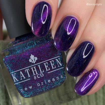 Nail polish with purple glitter finish held by a hand, showing brand &