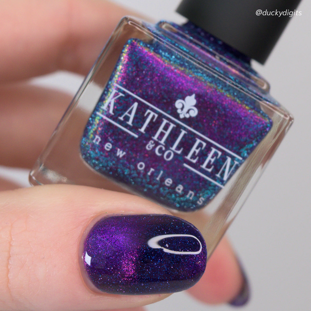 Nail polish bottle with glittery purple nail color on a finger, brand &