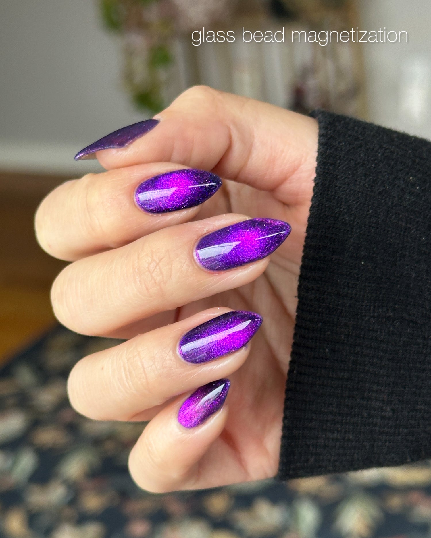 Hand with purple glass bead magnetized nails against a blurred background