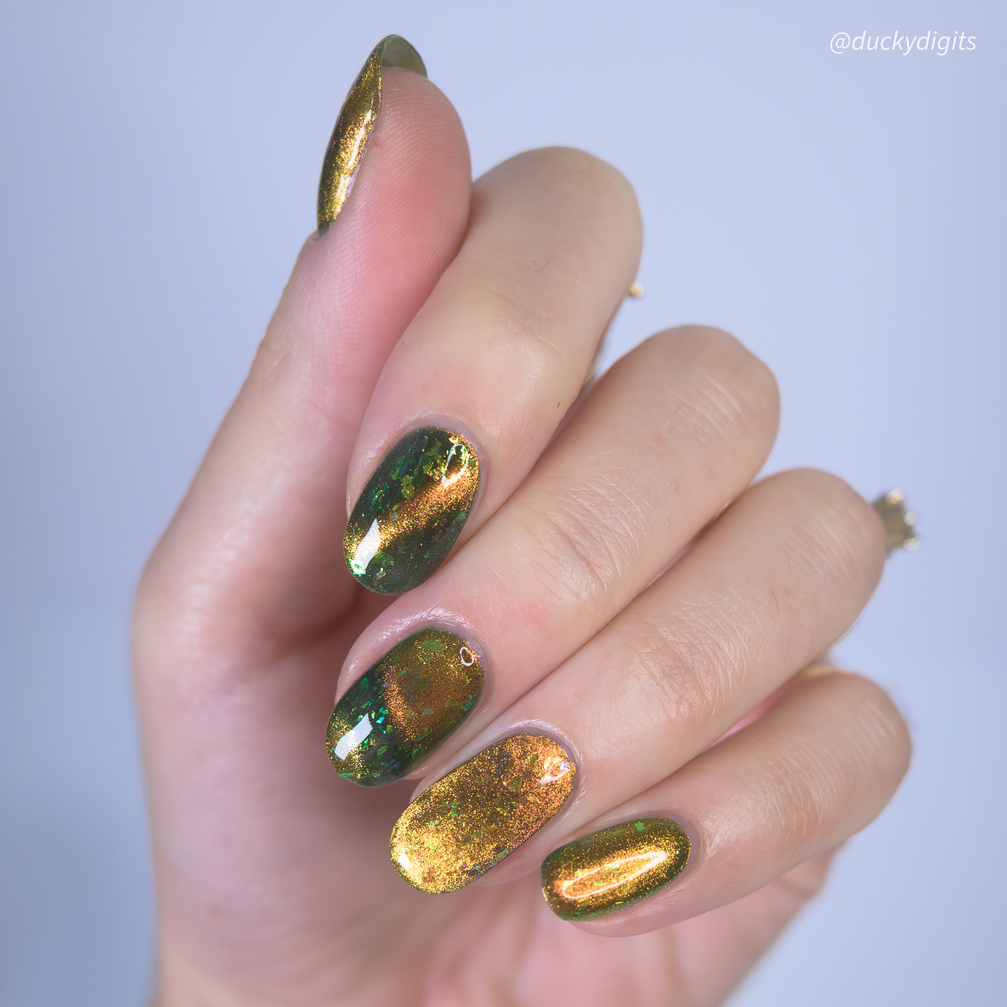 Hand with green and gold metallic magnetic nail polish on a light gray background