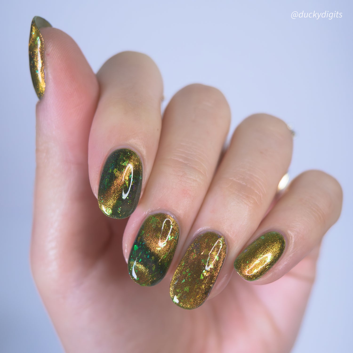Hand with green and gold magnetic nail polish on a white background