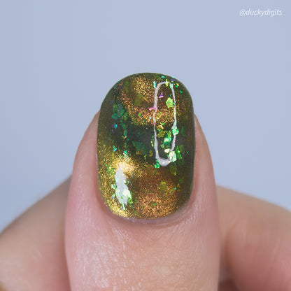Nail with green and gold cat eye nail polish on a light gray background