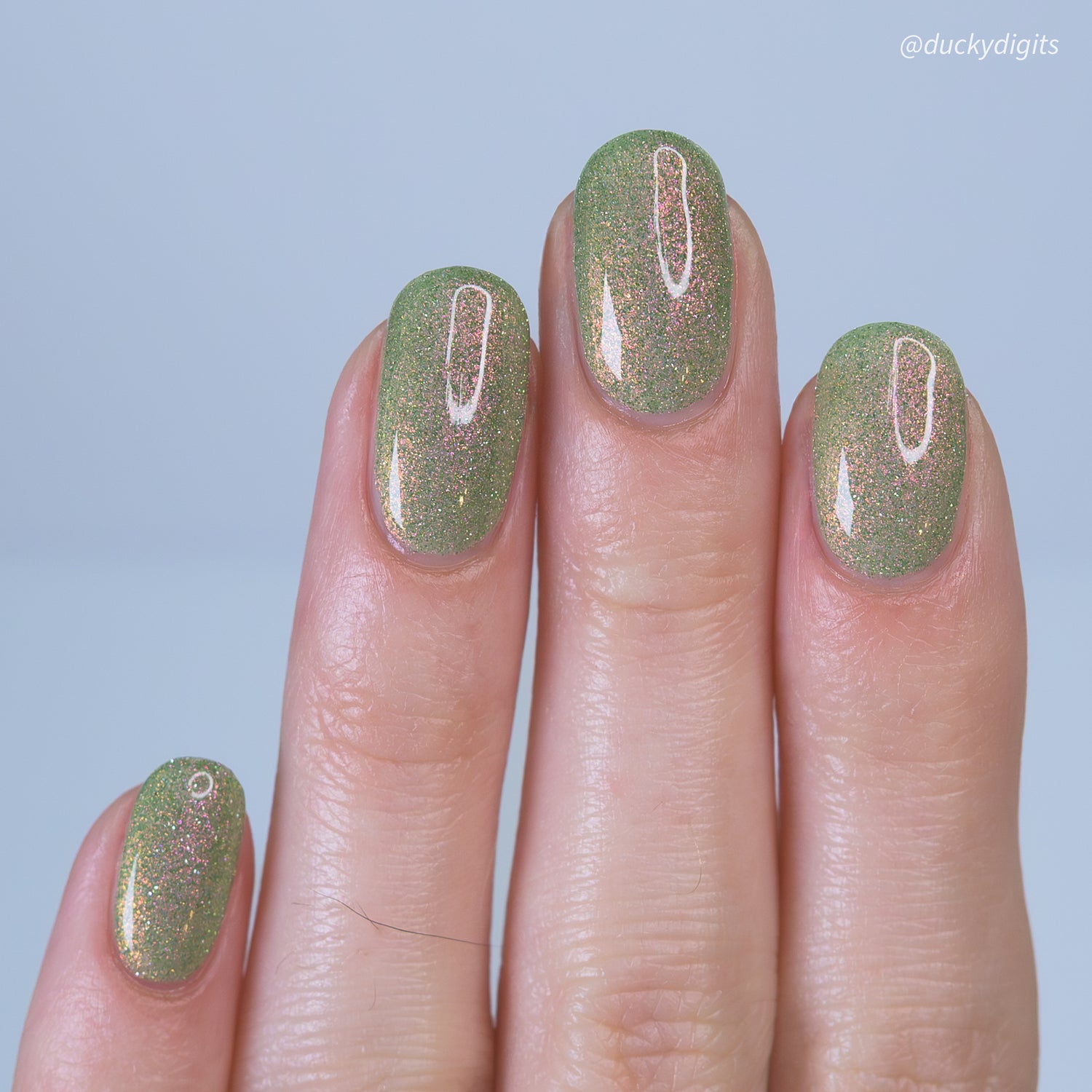 Nails with green reflective glitter nail polish on a light blue background