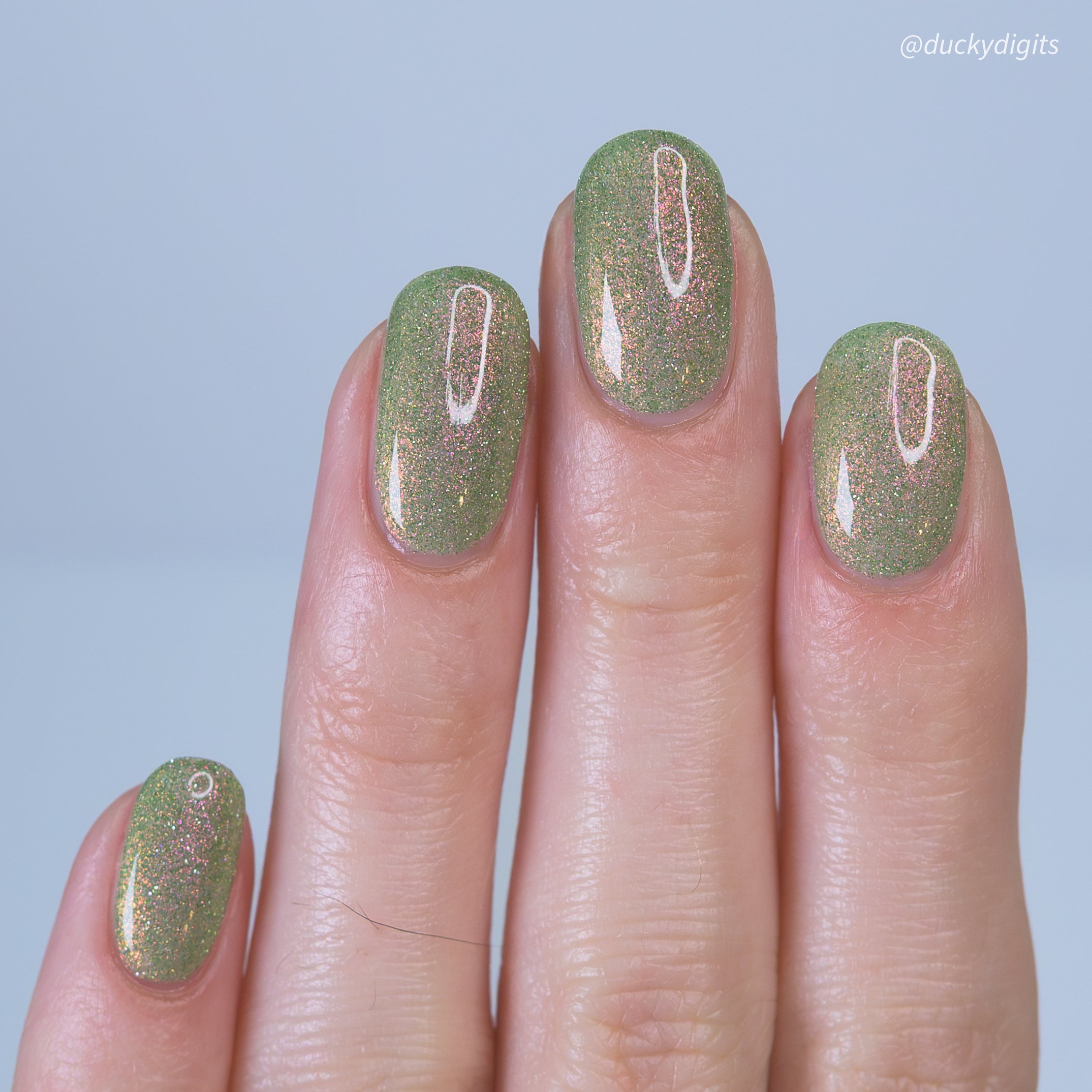 Nails with green reflective glitter nail polish on a light blue background