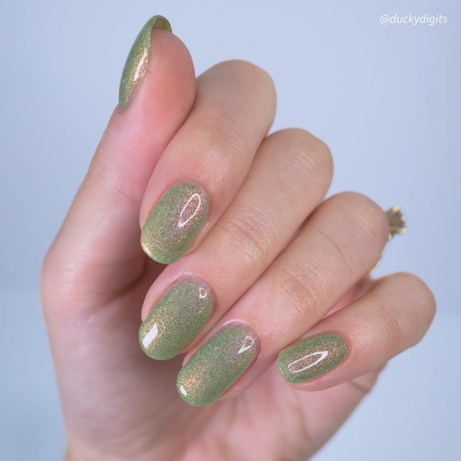 Hand with green glitter nail polish on a light blue background