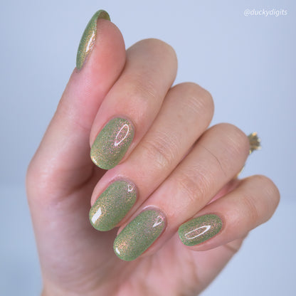 Hand with green glitter nail polish on a light blue background