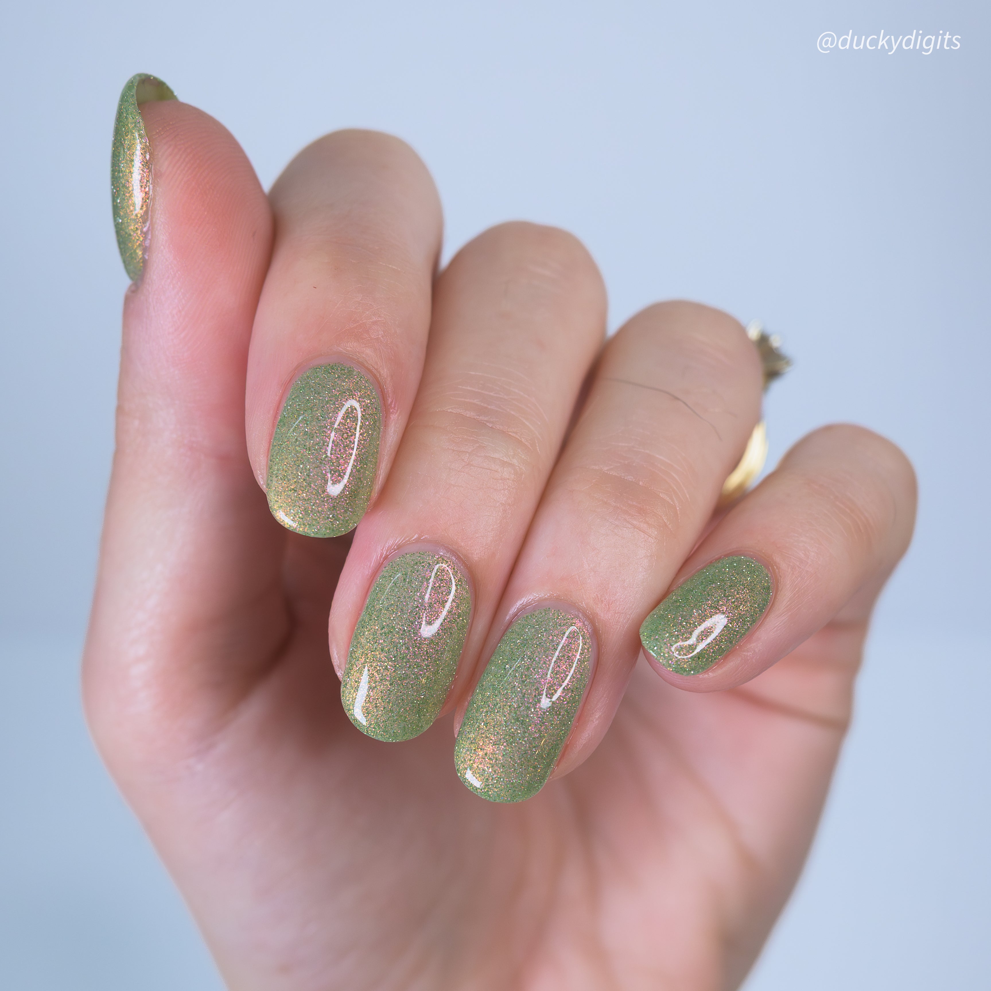 Hand with greenreflective glitter nail polish on a light gray background