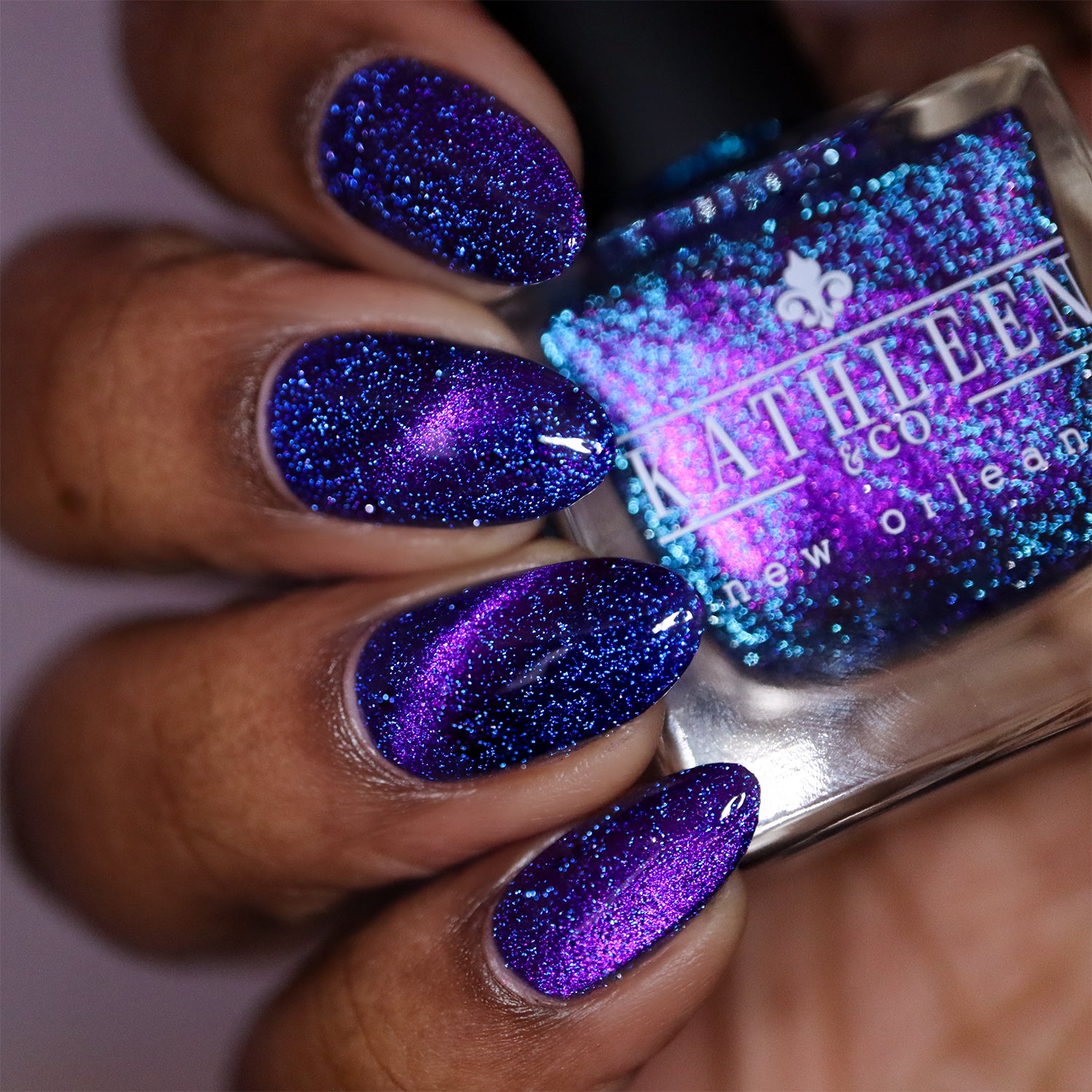 Hand with purple reflective glitter nails holding a bottle of Kathleen &amp; Co. nail polish.